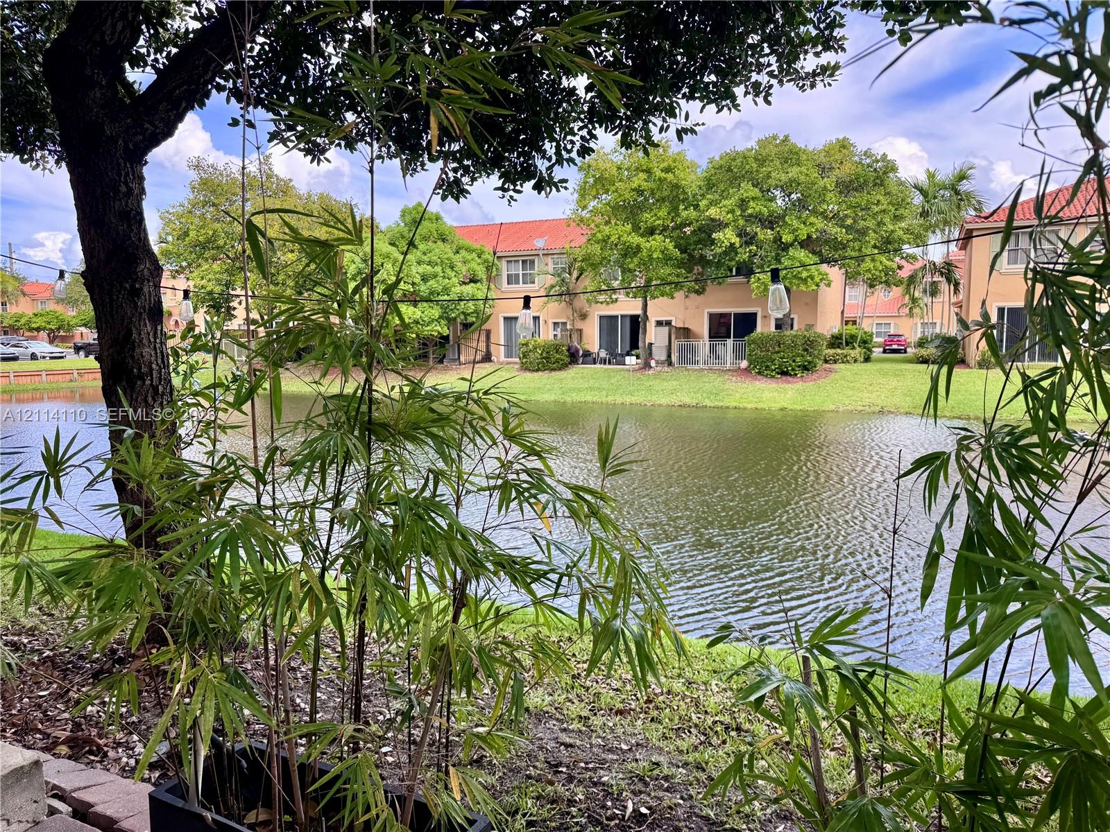 Waterfront grounds featuring a pond, mature trees, manicured lawn, and terracotta-style roof tiles