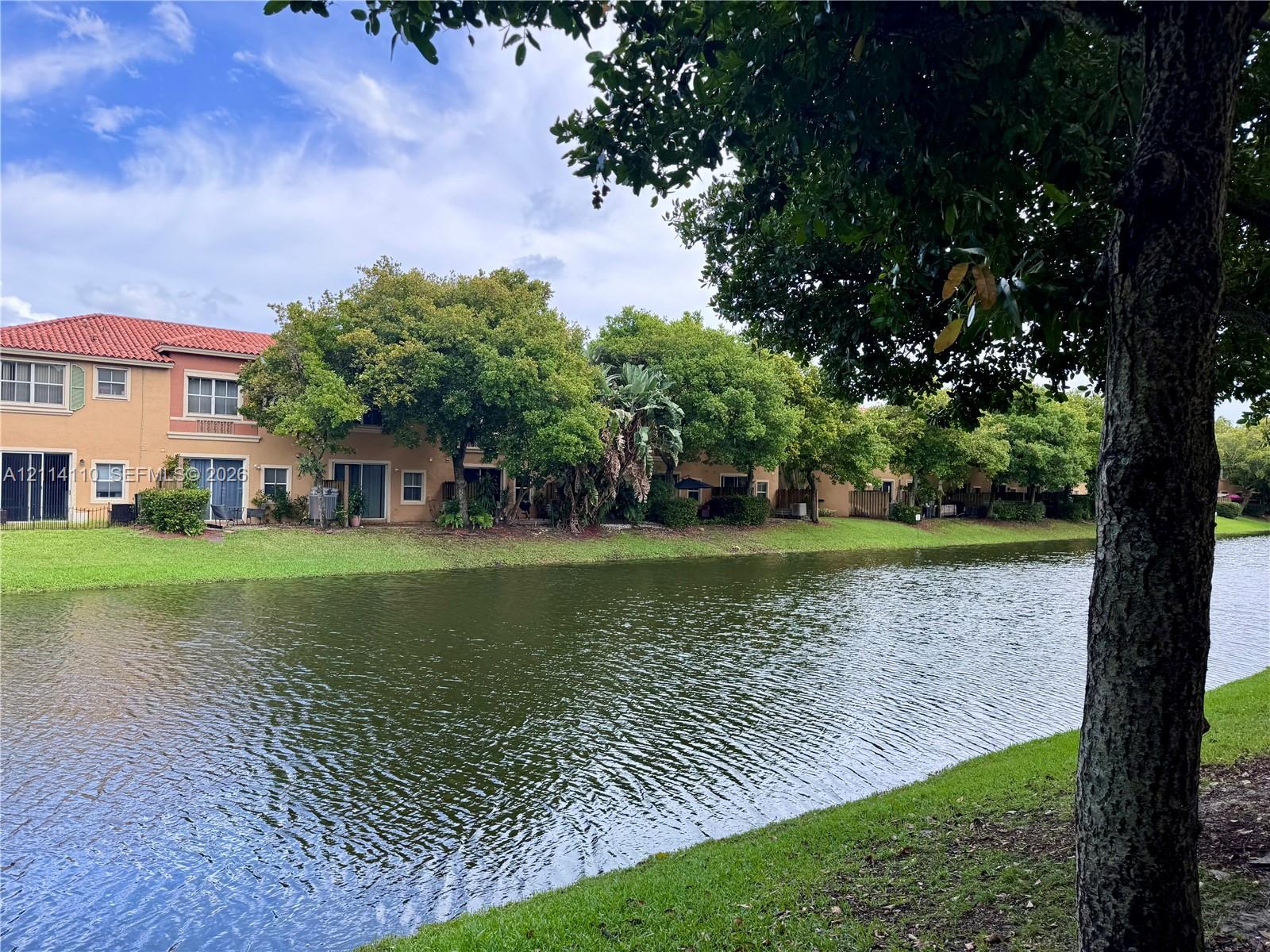 Waterfront exterior featuring a terracotta-tile roof, stucco facade, sliding glass doors, and expansive green space with mature trees Waterfront exterior featuring a terracotta-tile roof, stucco facade, sliding glass doors, and expansive green space with mature trees