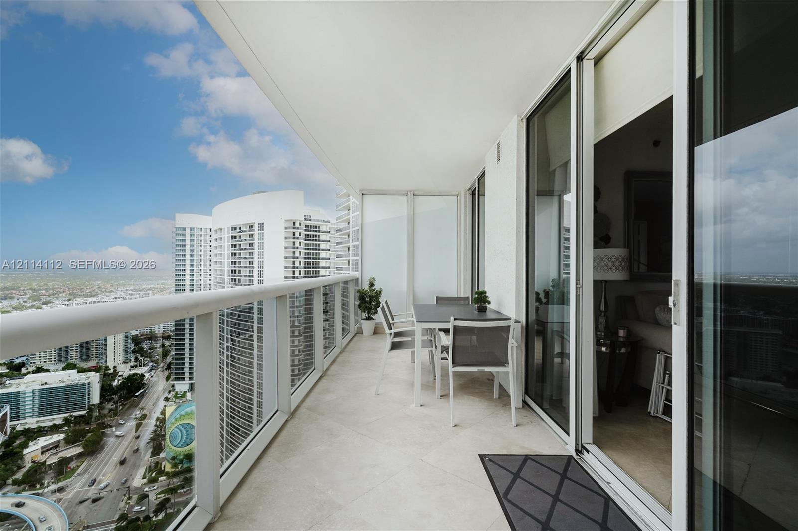 Covered balcony with stone-finish flooring, glass panel railings, and full-height sliding glass doors
