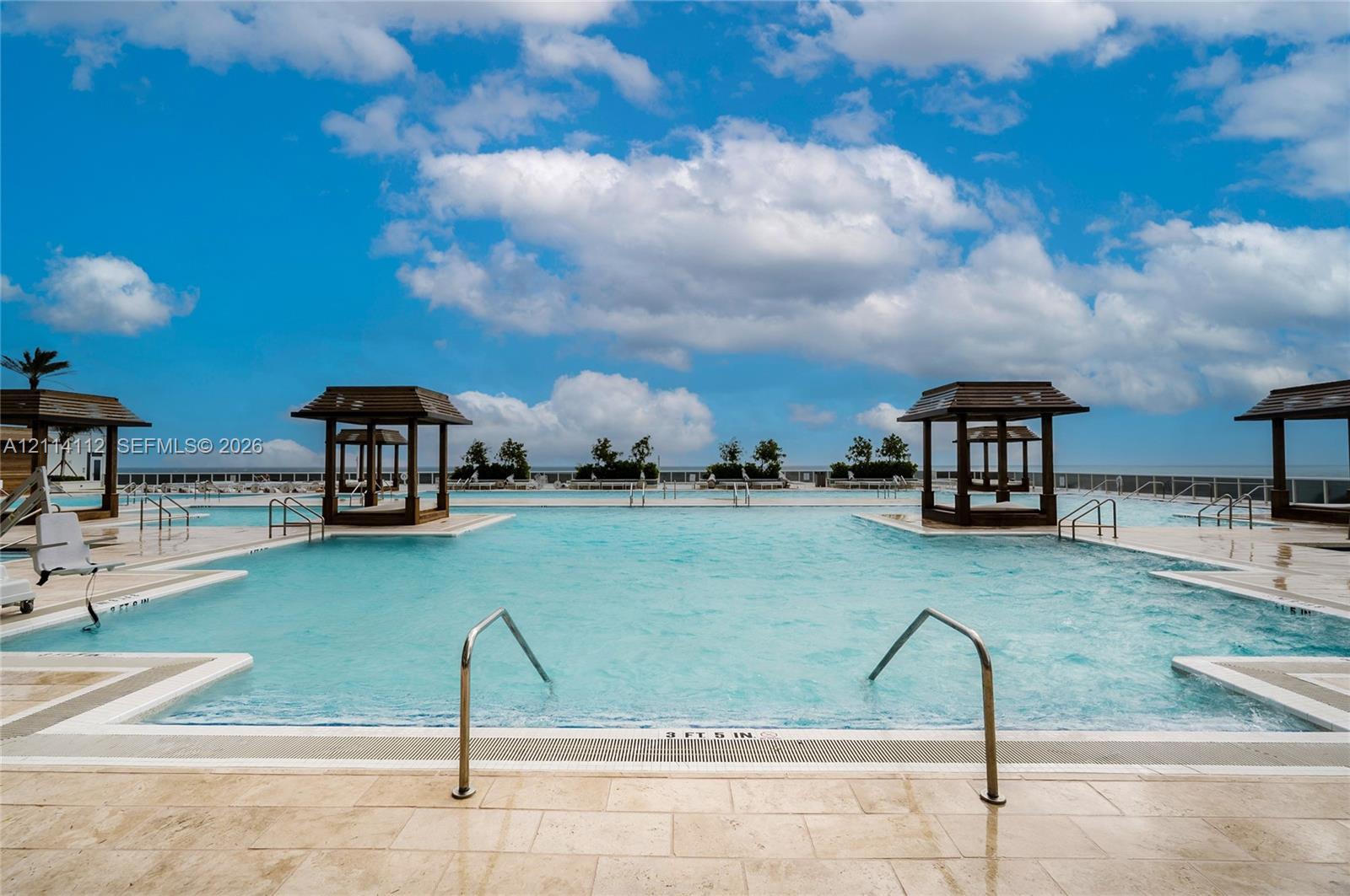 Expansive swimming pool featuring built-in wooden cabanas, stone paver decking, and metal handrails