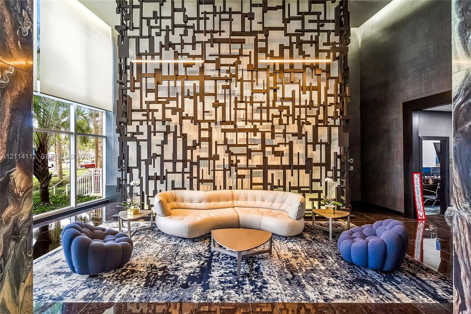 Lobby featuring a double-height ceiling, floor-to-ceiling windows, polished stone flooring, and a large-scale decorative geometric metal partition wall