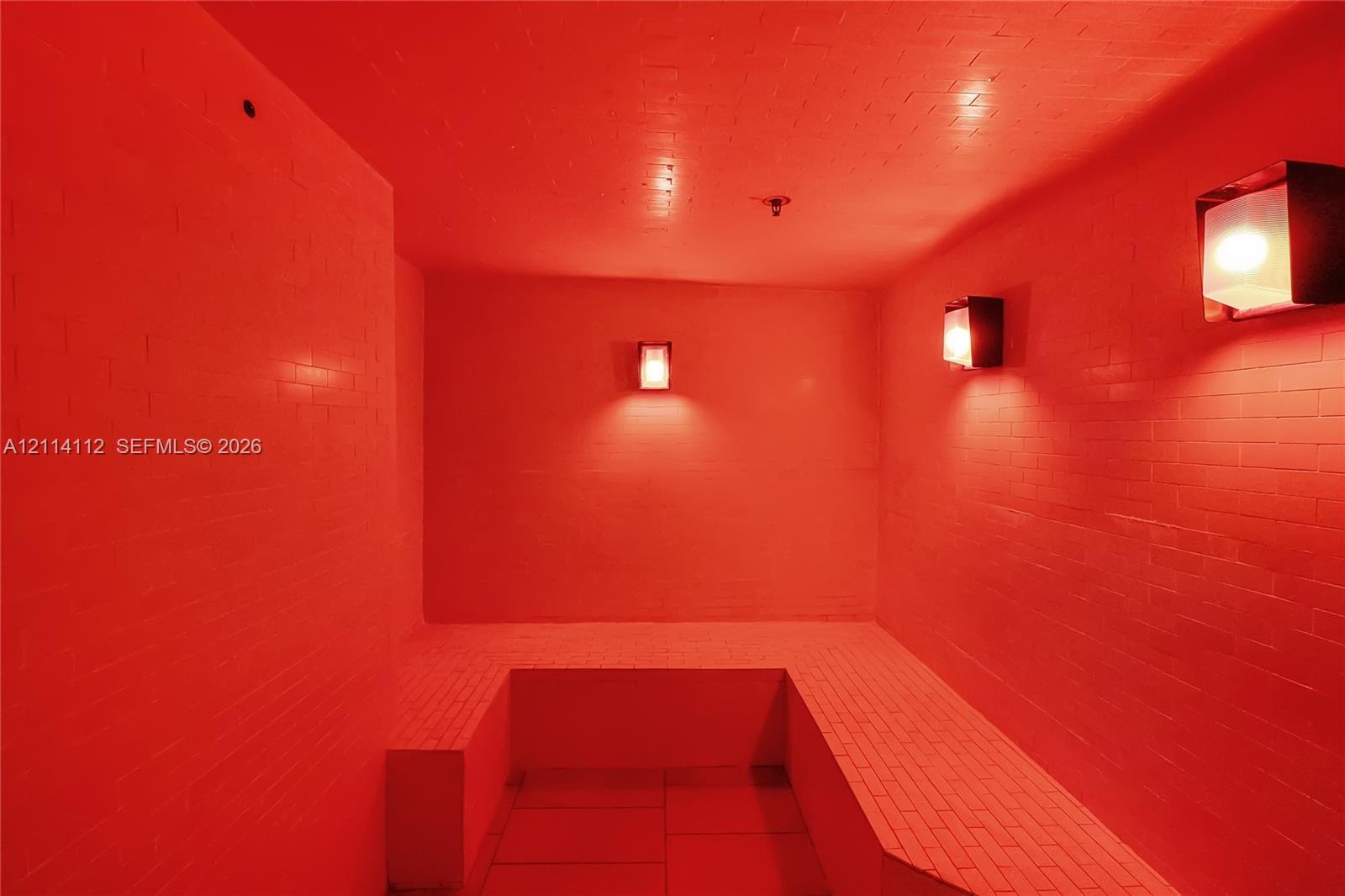 Enclosed room featuring floor-to-ceiling tiled walls, tiled bench seating, and two wall-mounted metallic light fixtures