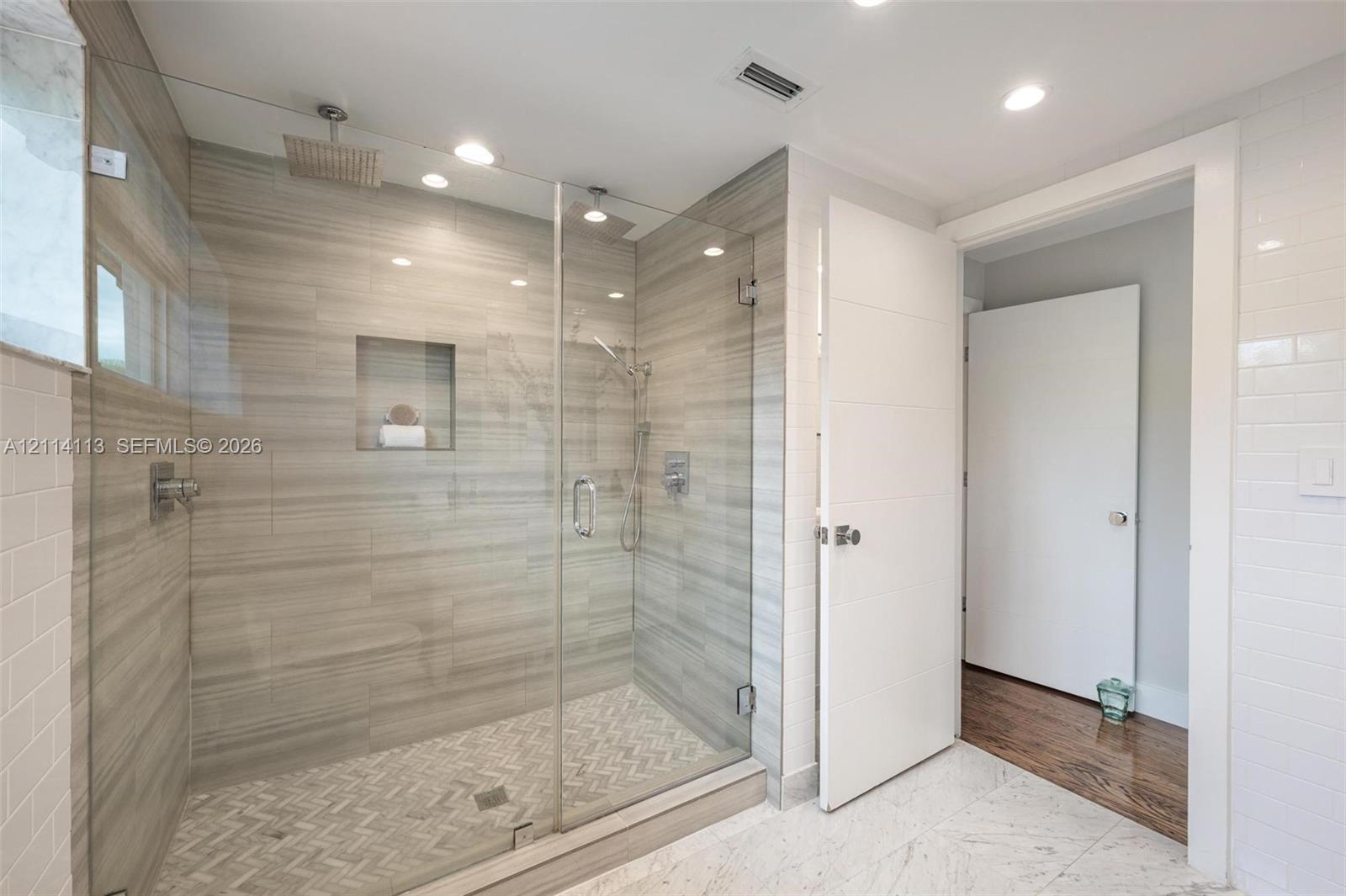 Walk-in shower featuring glass enclosure, ceiling-mounted rainfall showerhead, integrated tiled wall niche, and herringbone-patterned floor tile