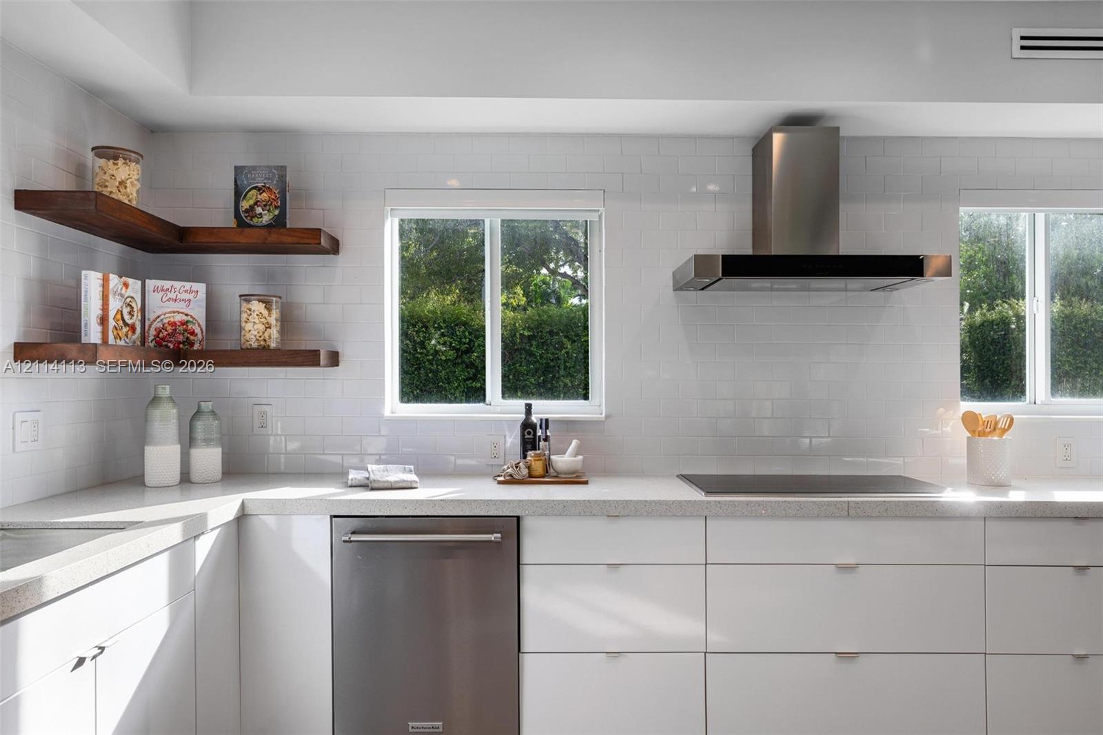 Kitchen featuring white flat-panel cabinetry, stone countertops, stainless steel appliances, a stainless steel range hood, and wood-finish floating corner shelves