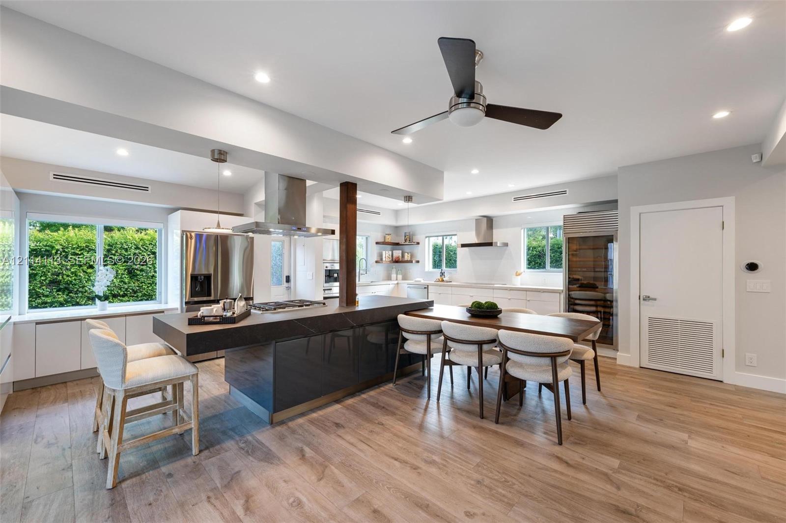 Gourmet kitchen featuring a large central island with stone-finish countertop, stainless steel appliances, wood-finish flooring, recessed lighting, and built-in wine storage