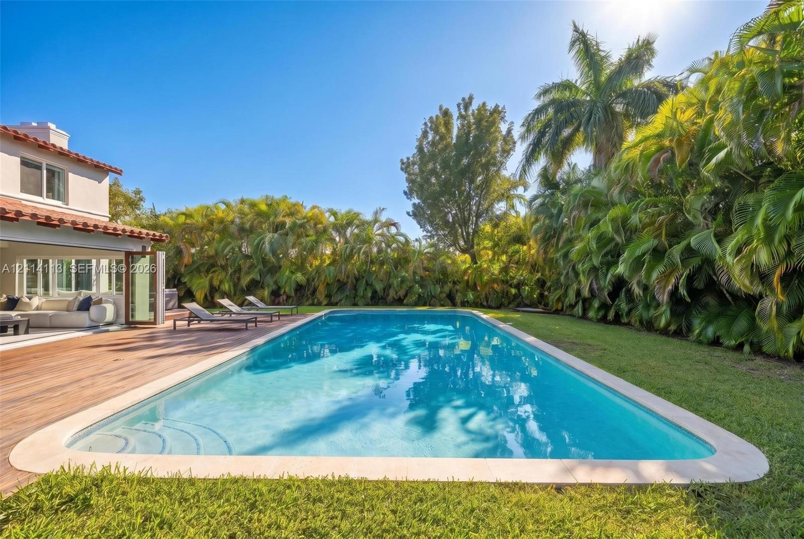 In-ground swimming pool with a stone coping border, wood-finish decking, and extensive perimeter greenery