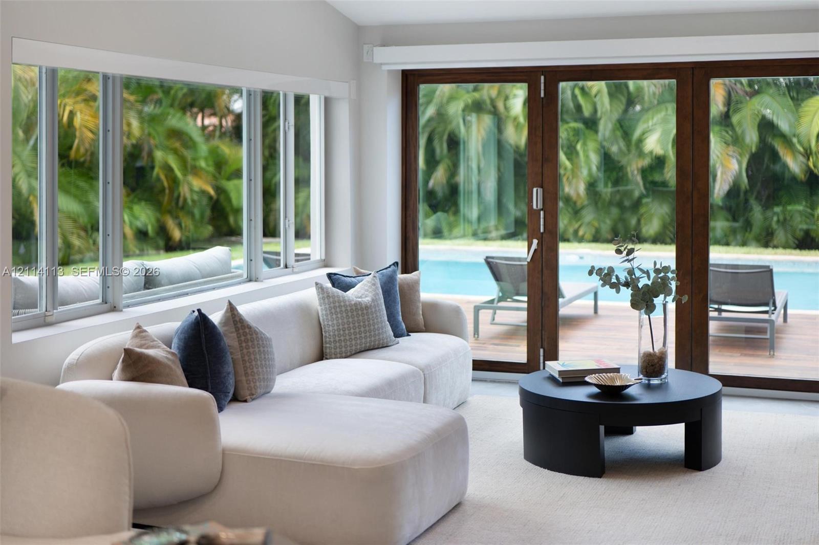 Expansive multi-pane windows and large-format sliding glass doors with dark wood frames, offering visibility to the outdoor pool and lush foliage