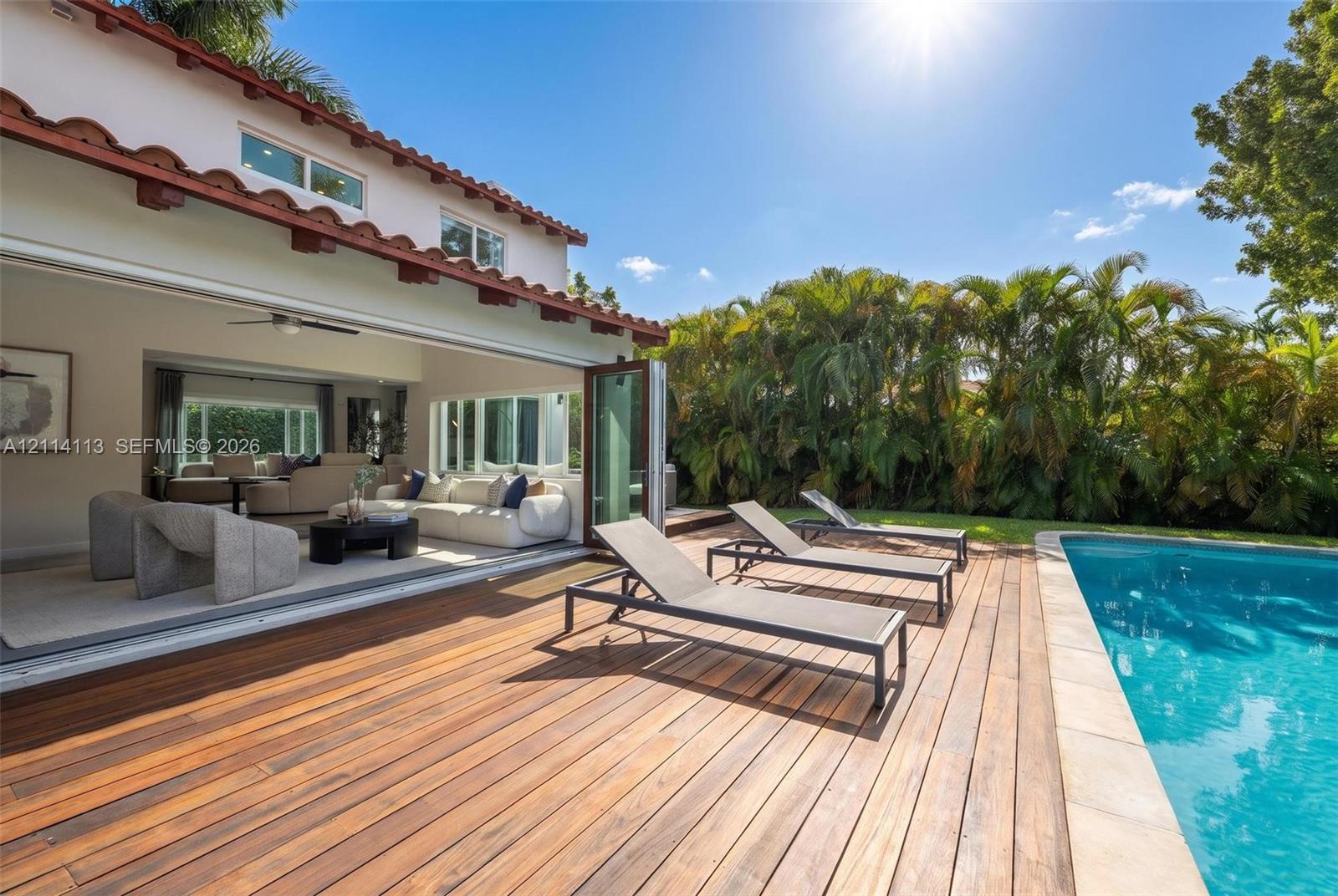 Exterior featuring wood decking, a swimming pool with stone coping, and expansive bi-fold glass doors