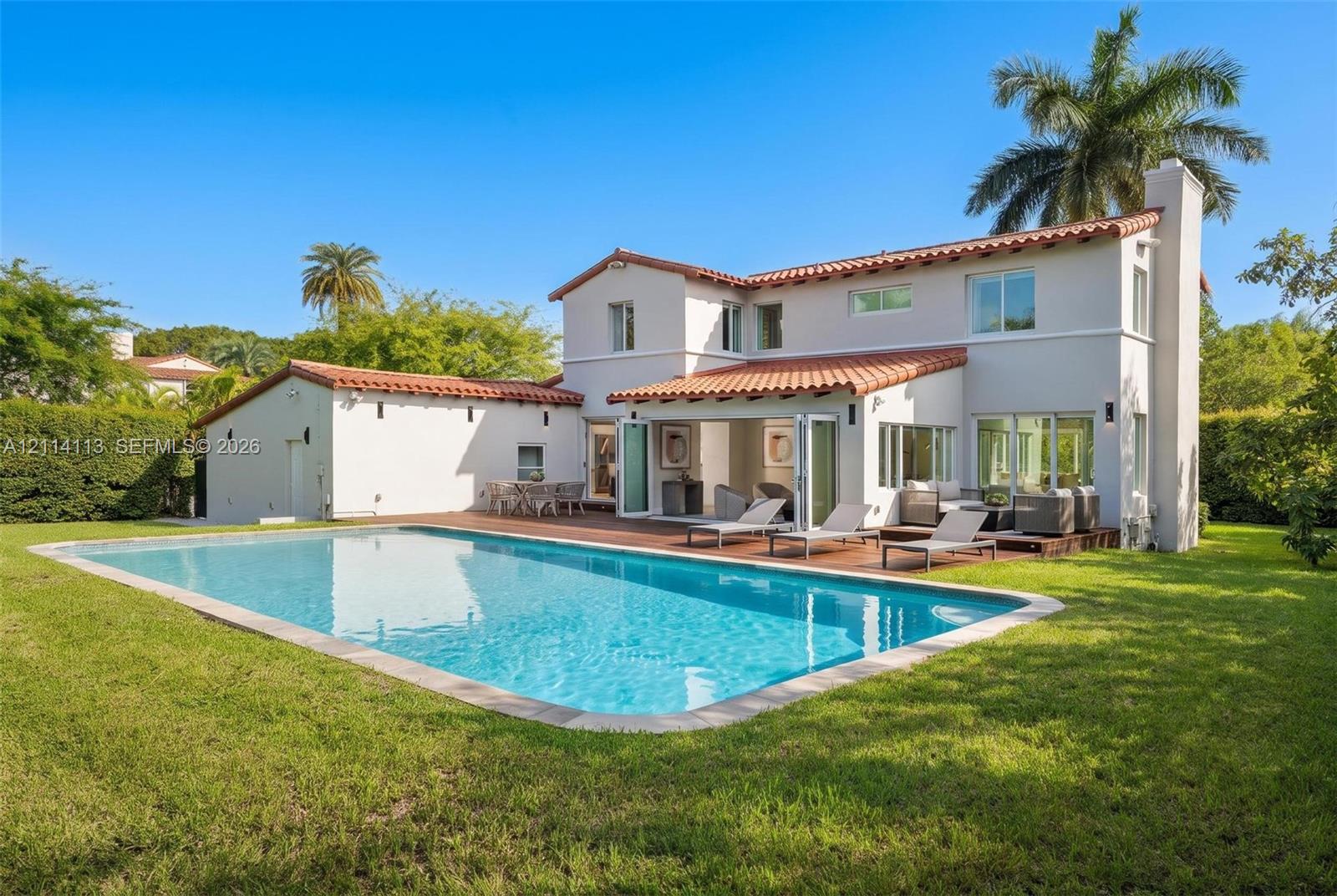 Mediterranean inspired exterior featuring a clay tile roof, stucco finish, in-ground swimming pool, wood-finish decking, and multi-panel folding glass doors