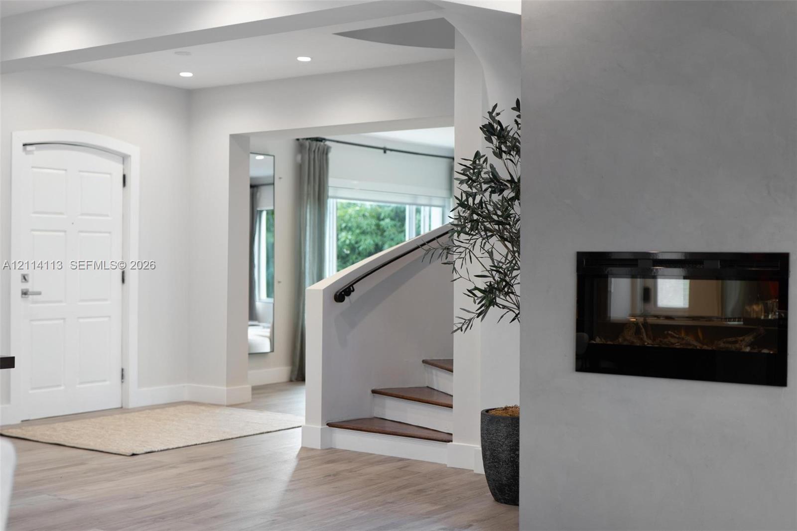 Foyer featuring recessed lighting, a recessed wall-mounted fireplace, a white arched-top entry door, and a staircase with wood-finish treads and a matte black handrail