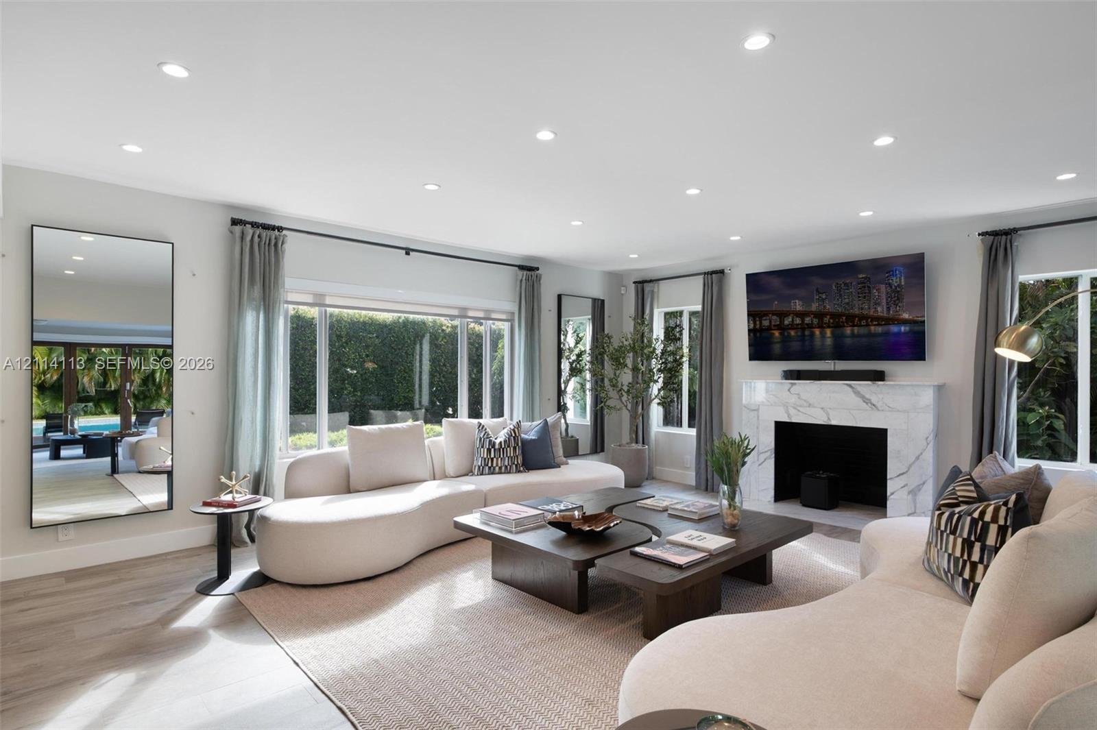 Spacious interior filled with natural light, featuring recessed lighting, stone-finish fireplace surround, large-format windows, and wood-finish porcelain flooring