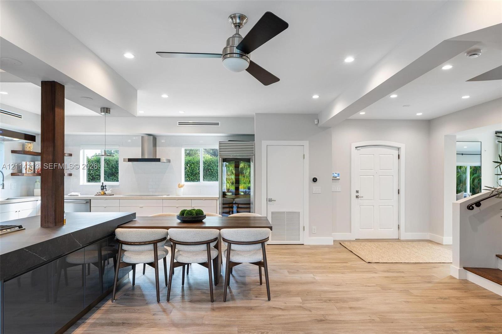 Open-concept interior featuring wood-finish flooring, recessed lighting, a modern ceiling fan, and a kitchen with a dark stone-top island and built-in cabinetry