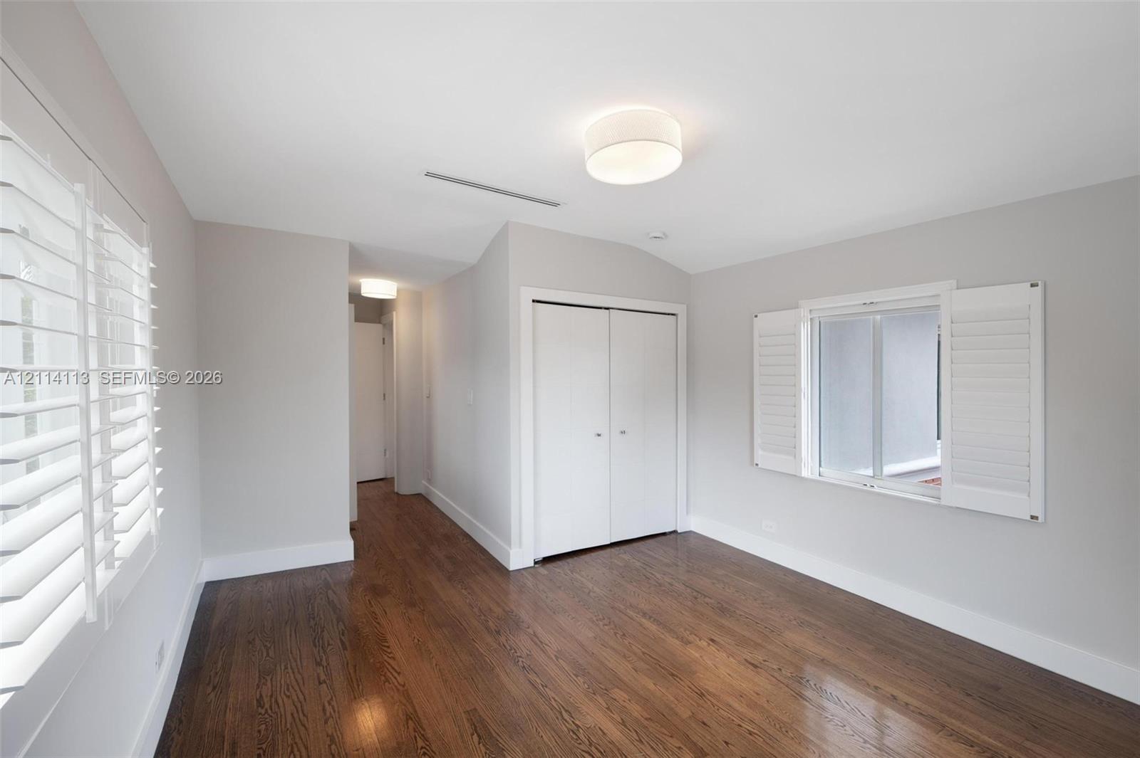 Room featuring wood-finish flooring, white plantation shutters, dual-door closet, and drum-style ceiling lighting