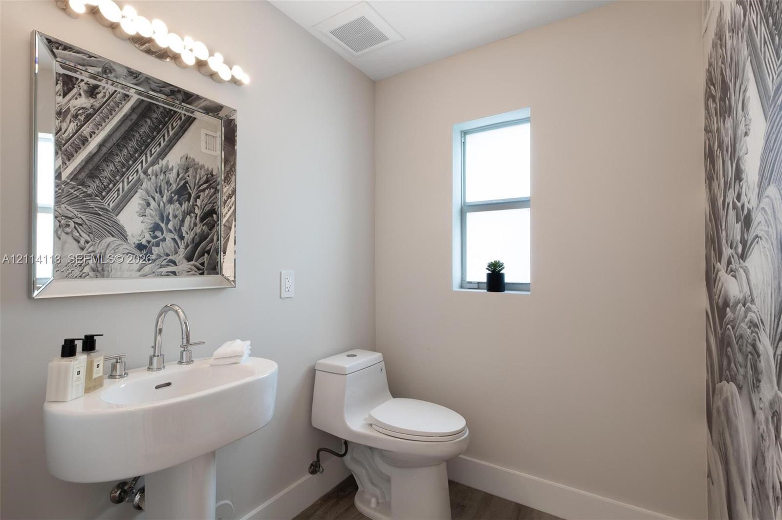 Pedestal sink with chrome faucet, multi-bulb vanity light, framed mirror, and toilet featuring a modern low-profile design