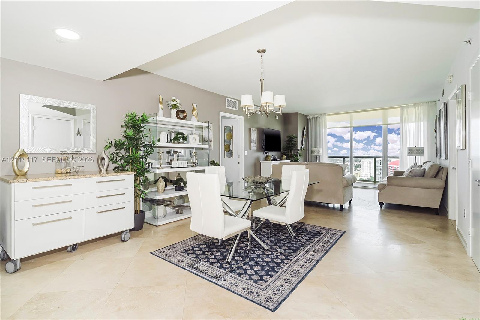 Open-concept living space featuring large-format tile flooring, a multi-arm chandelier, and floor-to-ceiling windows with access to an exterior balcony
