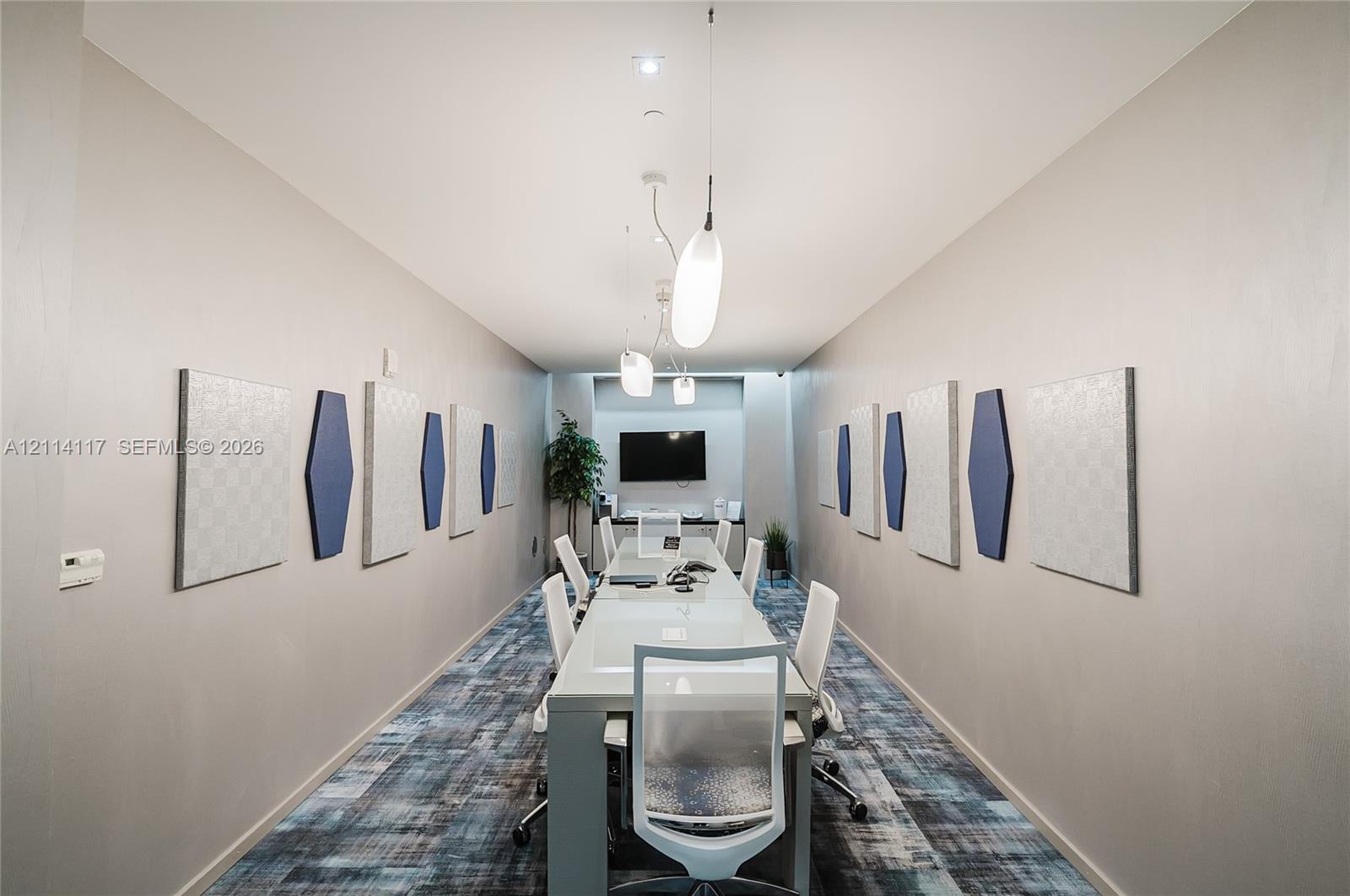 Conference room featuring patterned wall-to-wall carpeting, recessed ceiling lighting, elongated pendant fixtures, and decorative wall-mounted acoustic panels