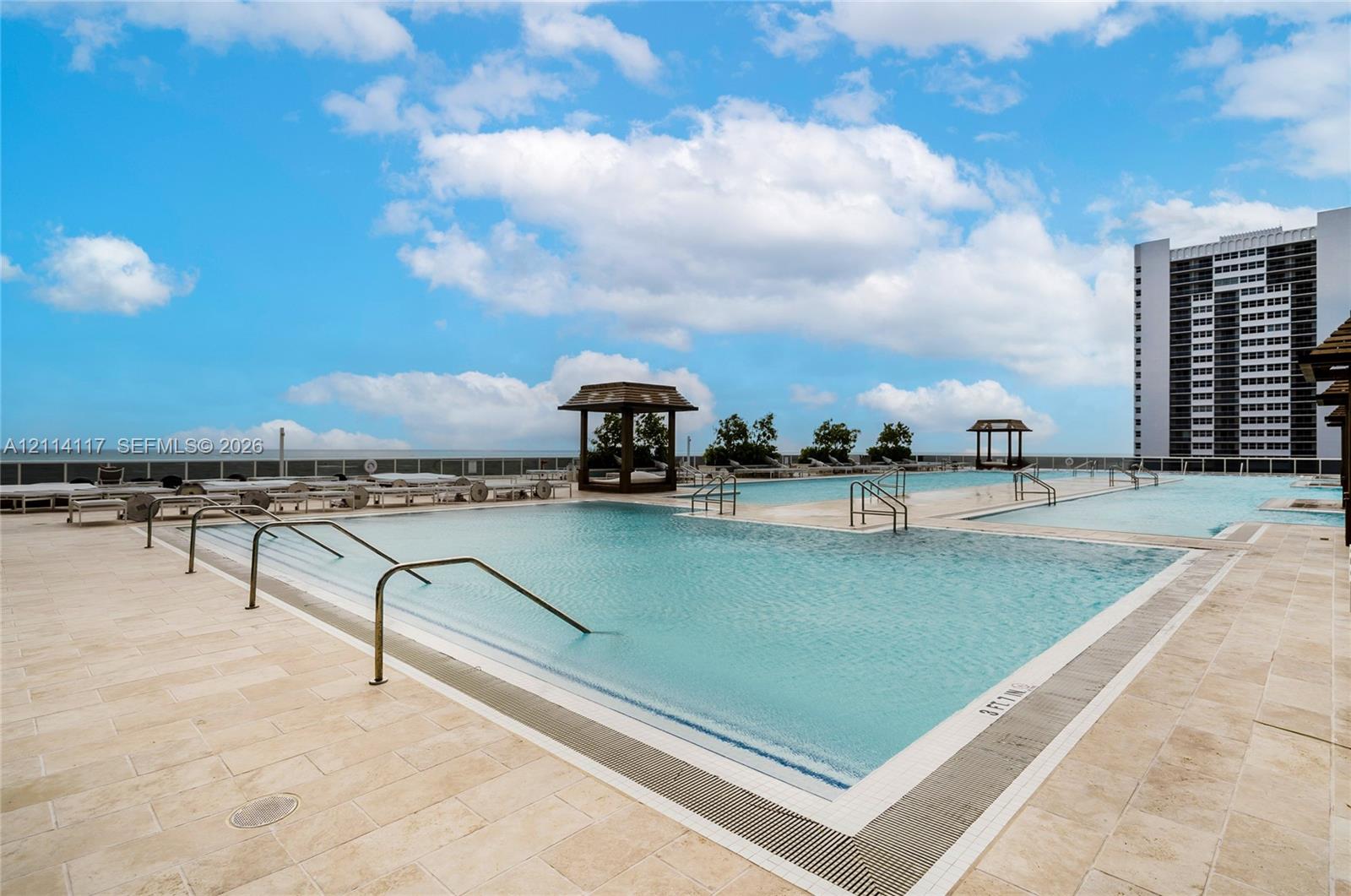 Multi-level swimming pool with stone-tiled decking, metal grab rails, and wooden shaded structures