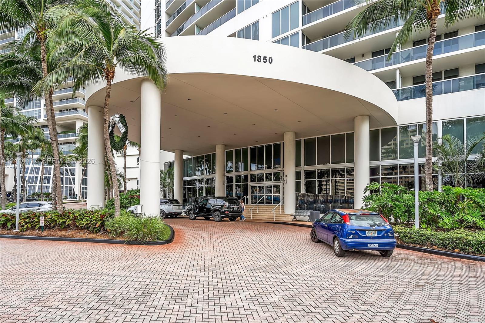 Covered motor court entrance featuring structural columns and a paver stone driveway