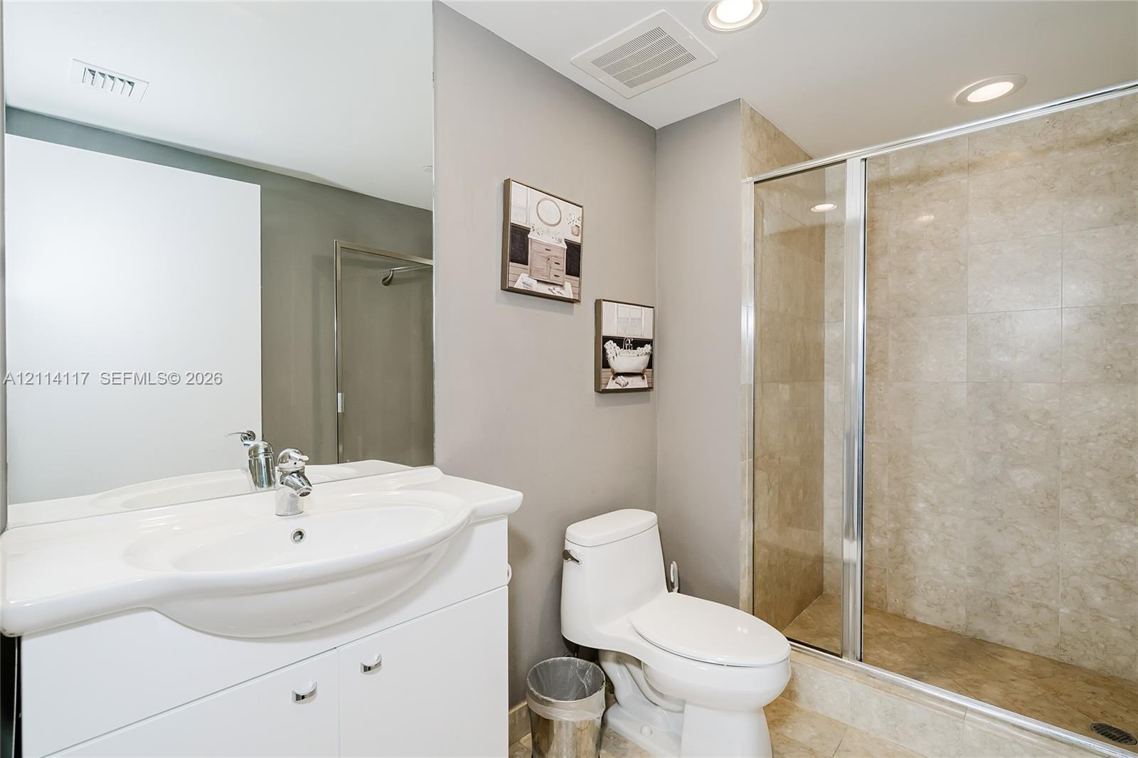 Bathroom featuring a white vanity with an integrated sink, a large wall-mounted mirror, a walk-in shower with stone-finish tile surround, and recessed lighting