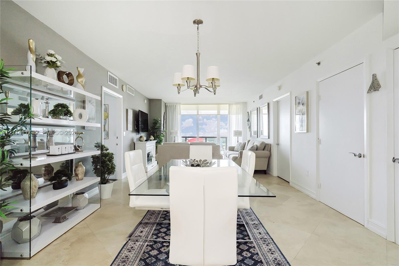 Open-concept room featuring neutral stone flooring, a multi-arm chandelier, built-in recessed display shelving, and full-height glass sliding doors