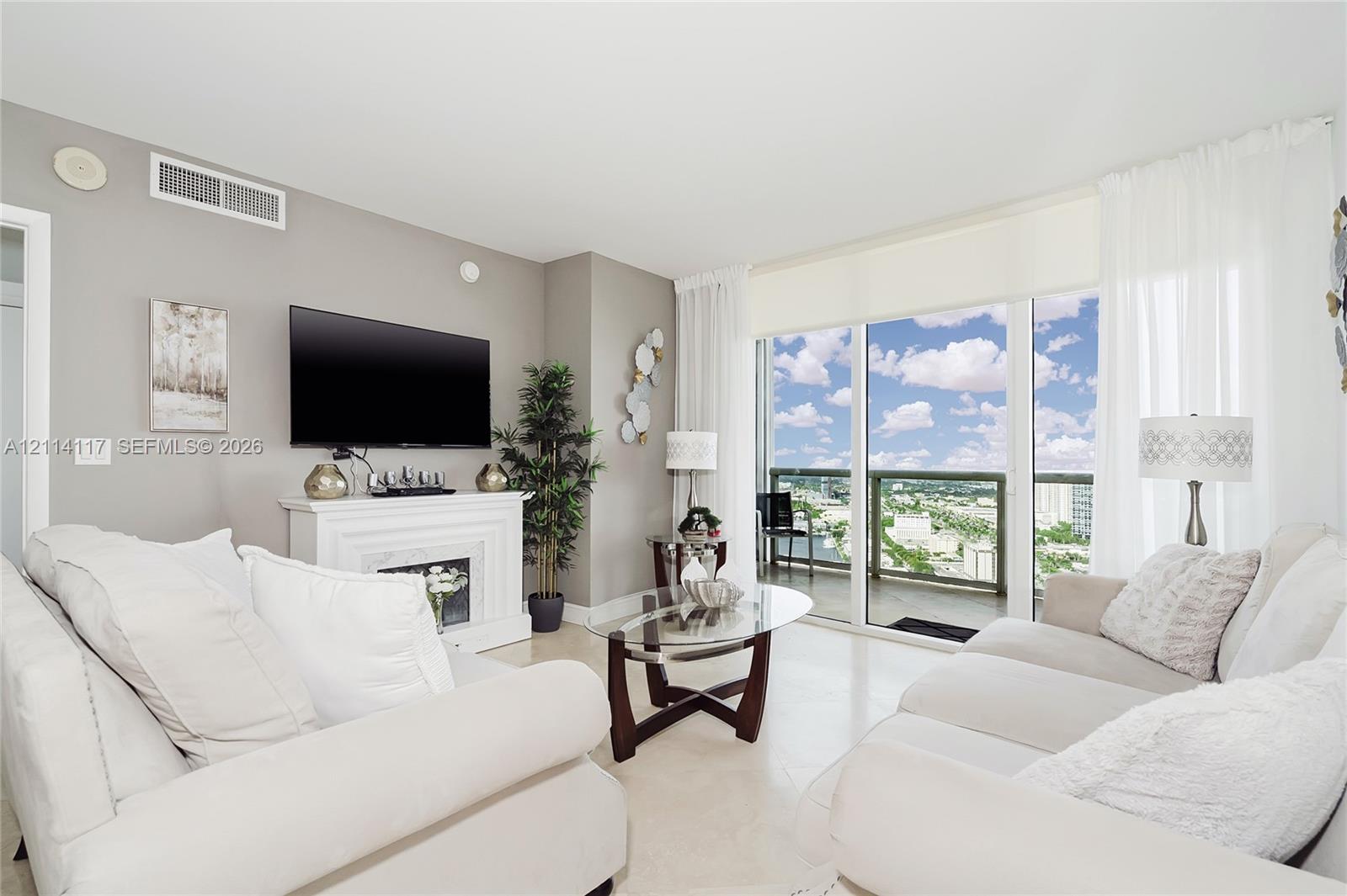Living area featuring neutral wall paint, tile flooring, a built-in decorative fireplace mantel, and full-height sliding glass doors opening to a balcony with glass railing