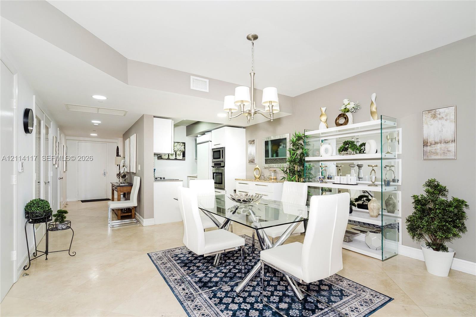 Open-concept dining area featuring neutral tile flooring, a multi-light metal chandelier, recessed ceiling lighting, and a built-in glass shelving unit