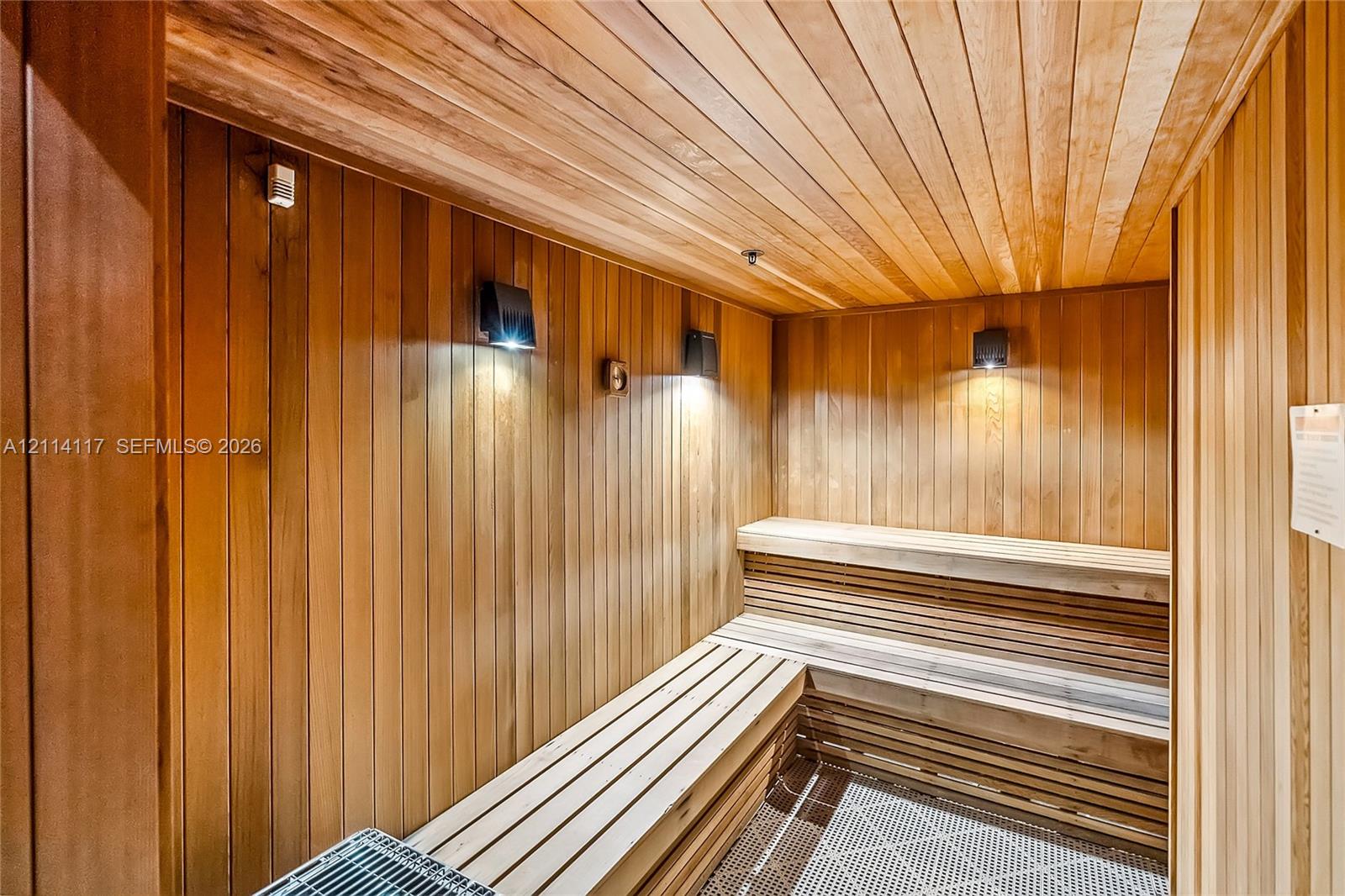 Sauna featuring natural wood tongue-and-groove wall and ceiling paneling, multi-level slatted wood benches, recessed wall-mounted sconce lighting, and a metal heating unit