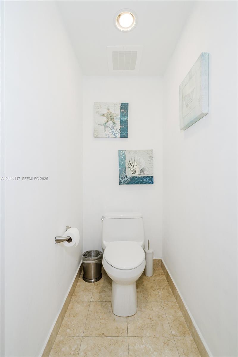 White dual-flush toilet, recessed ceiling lighting, and neutral-toned floor tiling