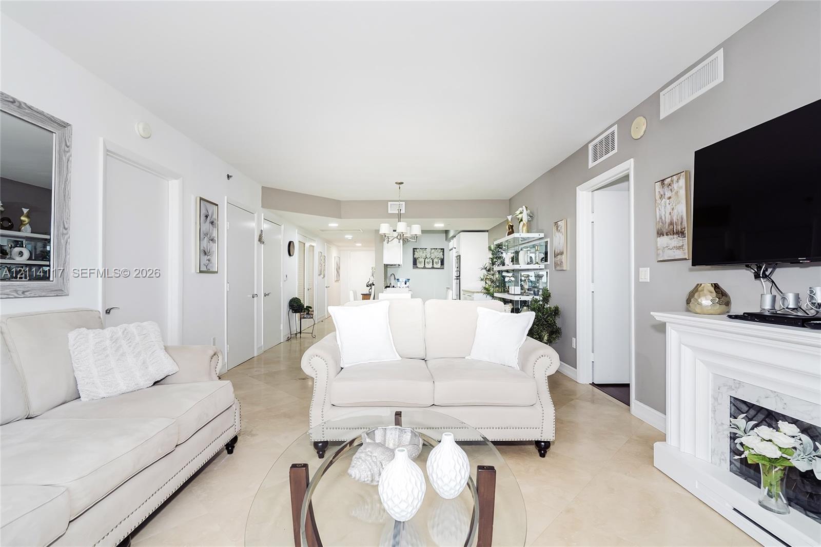 Open-concept interior featuring large-format neutral tile flooring, a built-in fireplace with detailed surround, and recessed ceiling lighting