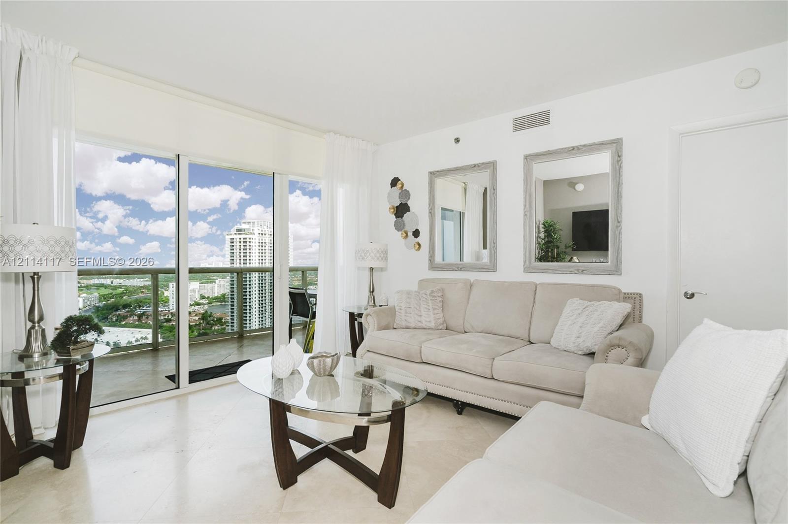 Living area featuring floor-to-ceiling glass sliding doors, stone-finish flooring, and a private balcony with glass railing