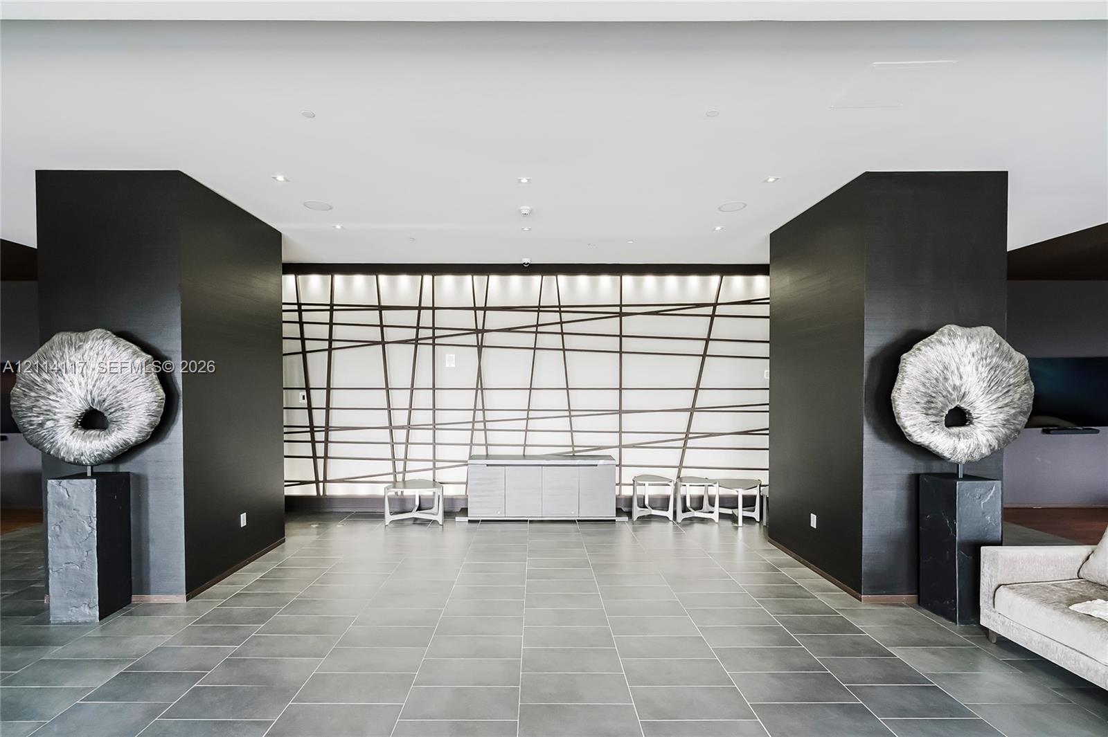 Interior space featuring oversized charcoal-toned structural columns, large-format matte tile flooring, and a decorative back-lit wall panel with geometric grid detailing