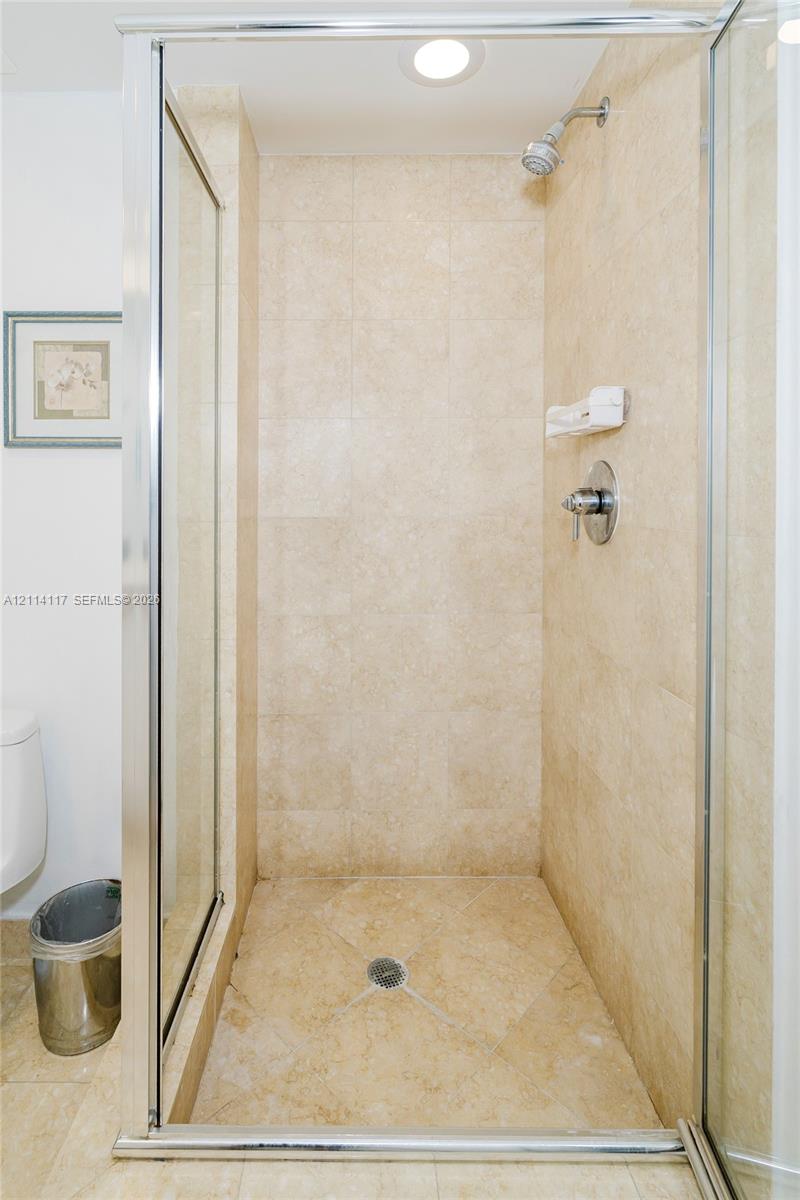 Walk-in shower enclosure featuring floor-to-ceiling tile, glass door with metal frame, integrated soap dish, and chrome plumbing fixtures