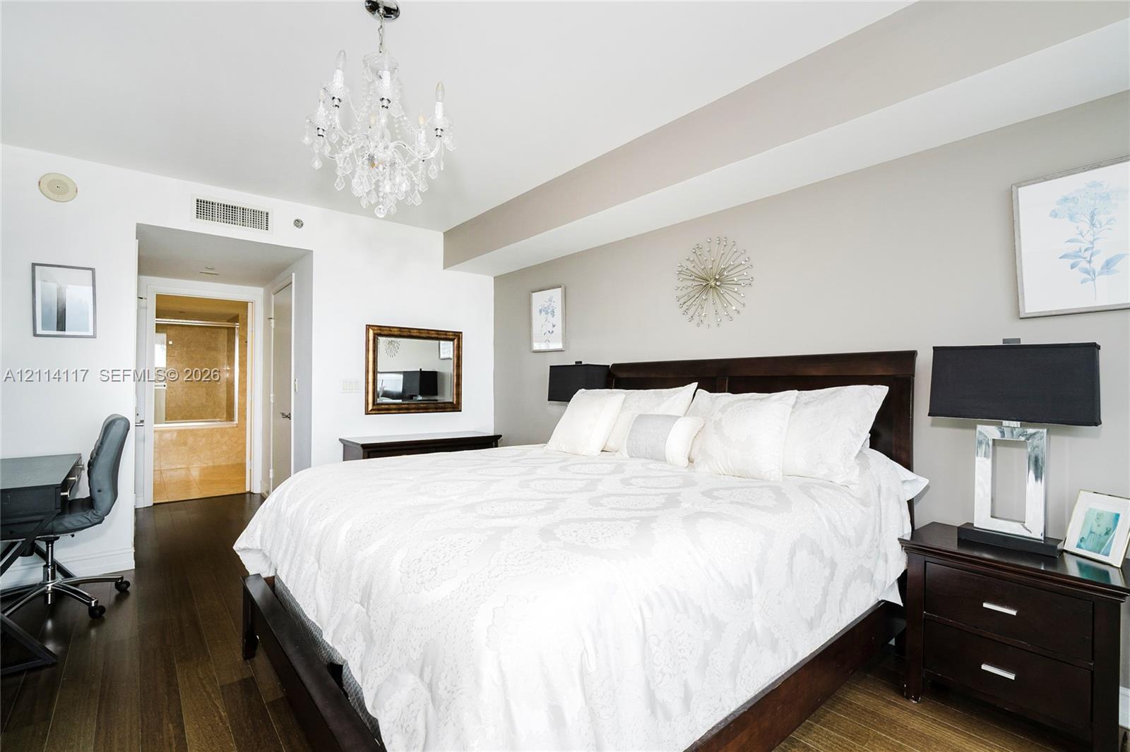 Room featuring dark wood-finish flooring, a tiered crystal chandelier, and a recessed ceiling architectural detail