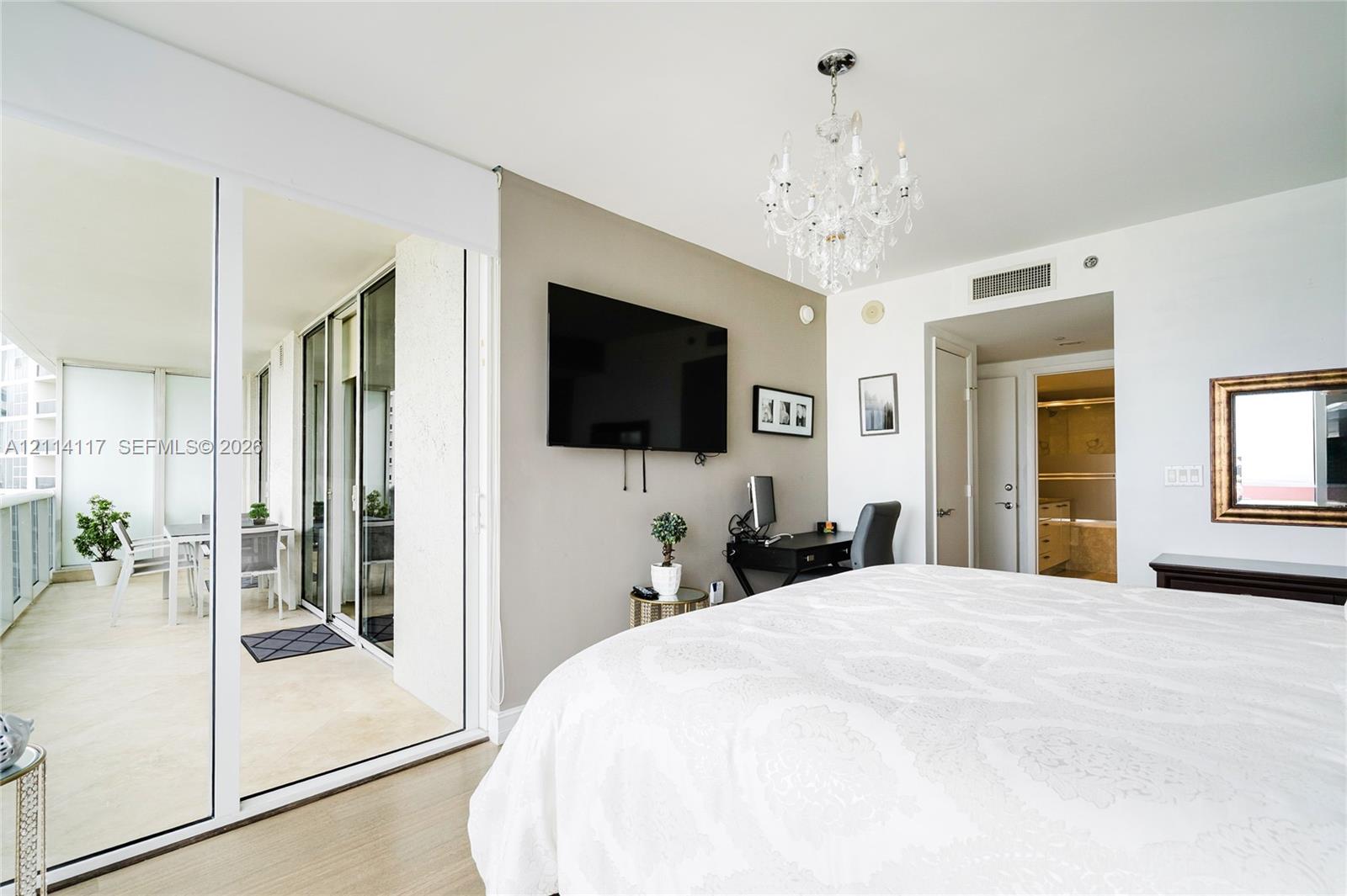 Floor-to-ceiling glass sliding doors opening to an expansive covered balcony, multi-light crystal chandelier, and light-toned wood-finish flooring