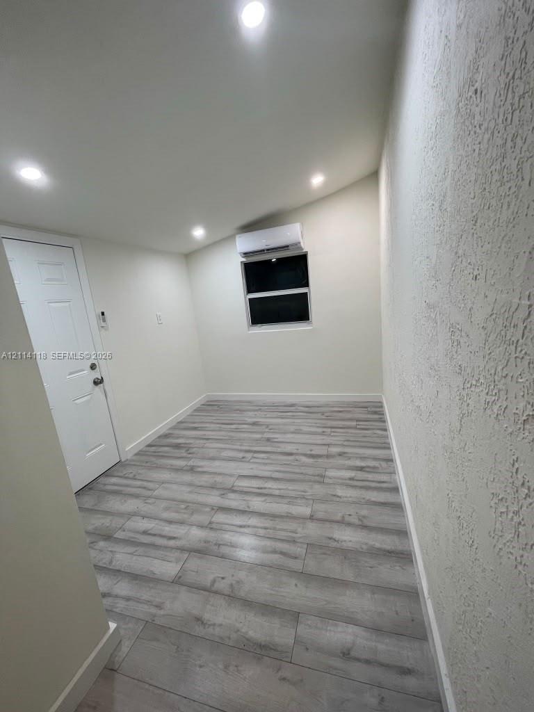 Interior room featuring wood-finish flooring, recessed lighting, a wall-mounted ductless mini-split unit, and a single-panel door