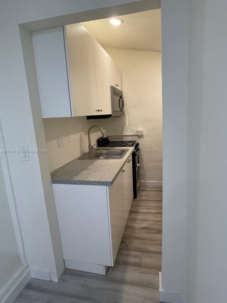 Kitchen featuring white cabinetry, stone-finish countertops, stainless steel sink with gooseneck faucet, integrated microwave, and wood-finish flooring