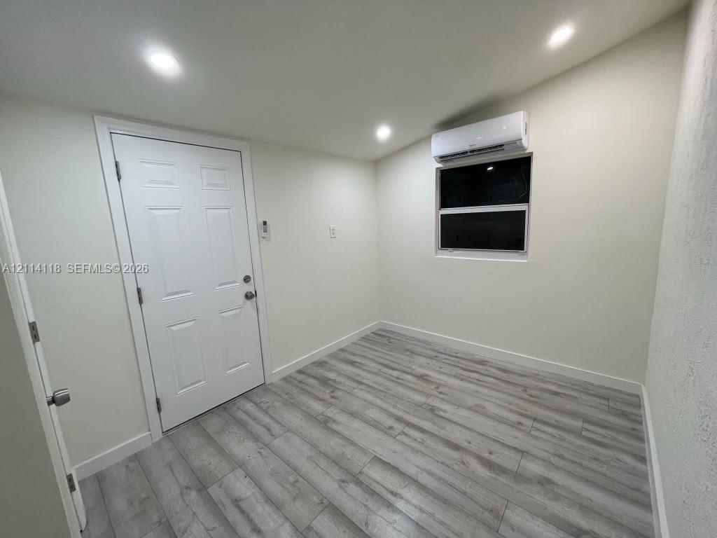 Interior space featuring wood-finish flooring, recessed lighting, wall-mounted climate control unit, and a single-hung window