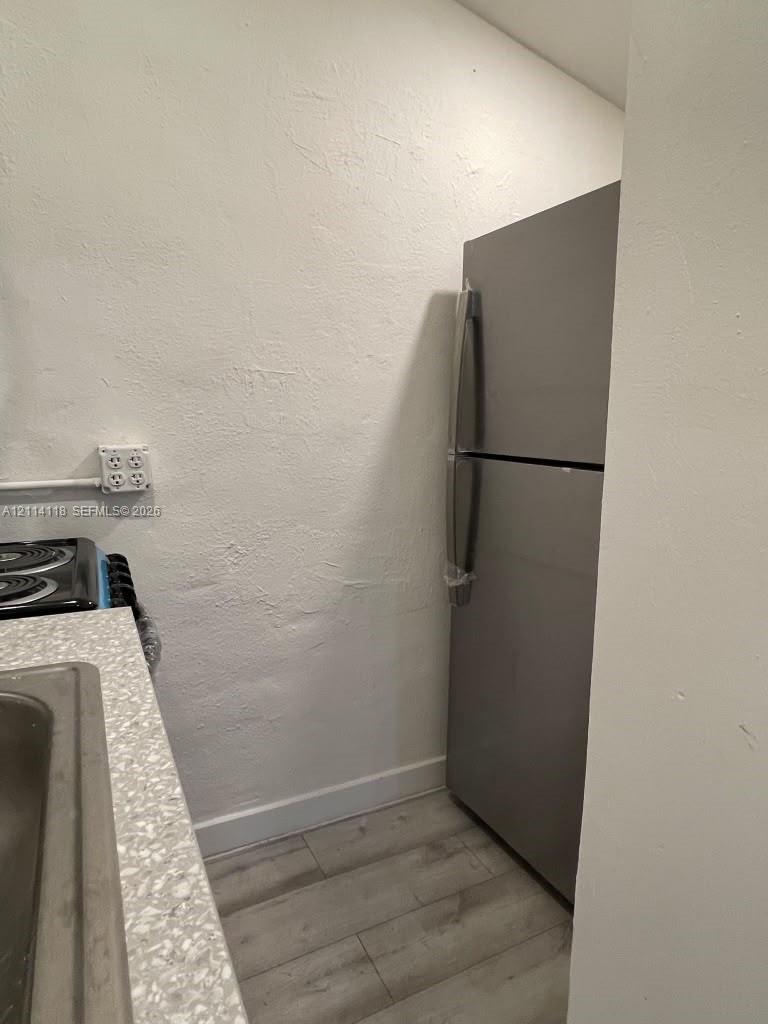 Stainless steel refrigerator, textured wall finish, speckled countertop, and wood-finish flooring