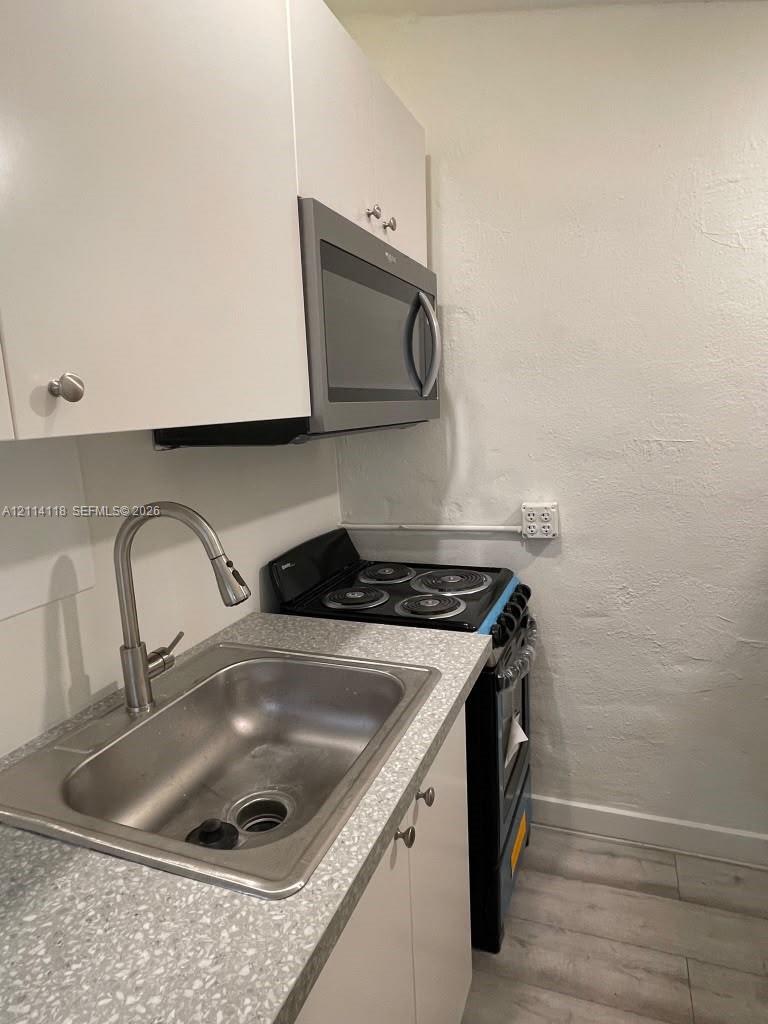 Kitchen featuring white cabinetry, a stainless steel sink with an arched pull-down faucet, a textured countertop, and a built-in microwave oven