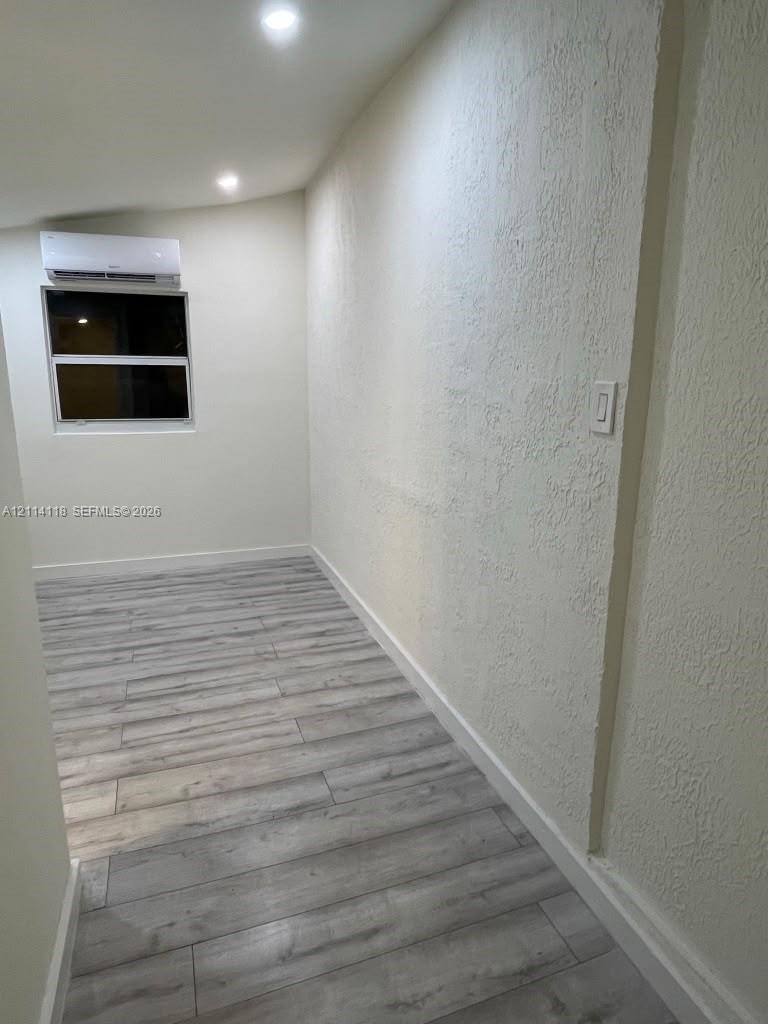 Room interior featuring wood-finish flooring, recessed lighting, and a wall-mounted ductless air conditioning unit