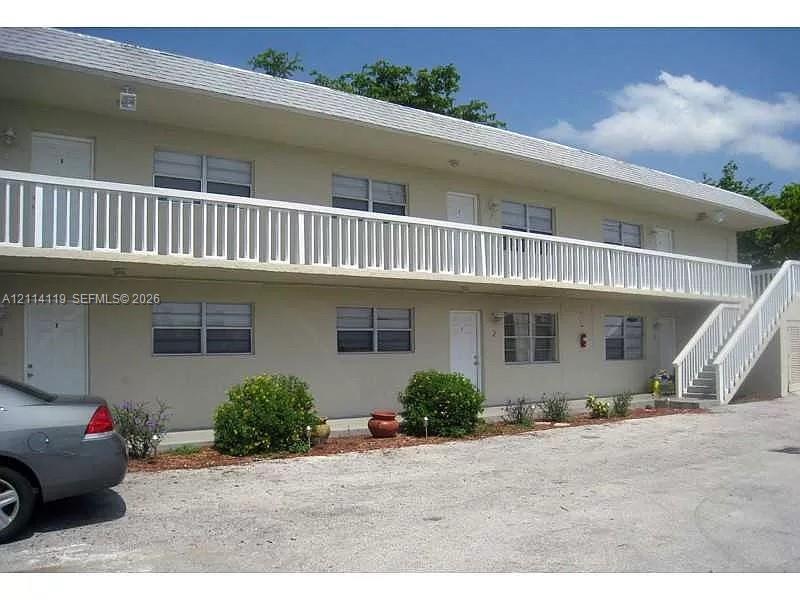 Two-story multi-unit exterior featuring a wide second-level balcony with white railings, external staircase, and horizontal sliding windows Two-story multi-unit exterior featuring a wide second-level balcony with white railings, external staircase, and horizontal sliding windows