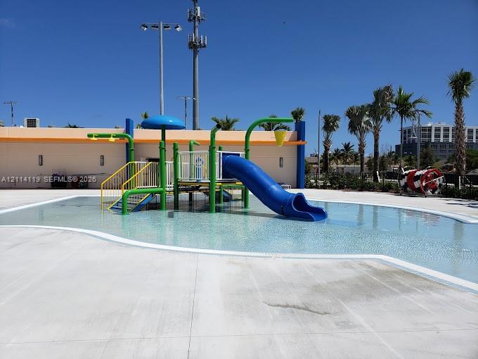 Water play area featuring a shallow-entry pool, integrated structure with a slide, overhead water features, and concrete decking