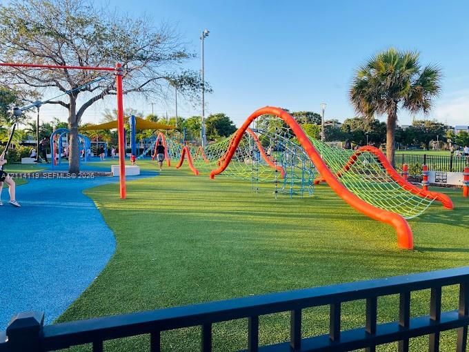 Recreational grounds featuring a structured climbing net, rubberized surfacing, mature trees, and perimeter metal fencing