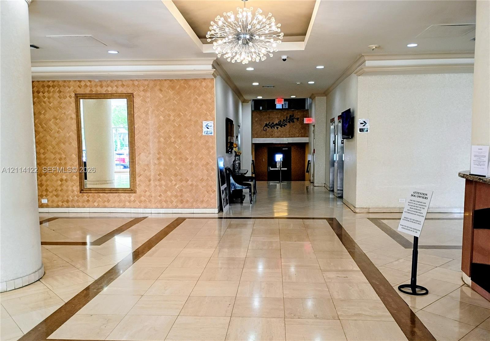 Lobby area featuring polished tile flooring with inlaid borders, a decorative recessed ceiling with a contemporary chandelier, and a textured accent wall Lobby area featuring polished tile flooring with inlaid borders, a decorative recessed ceiling with a contemporary chandelier, and a textured accent wall