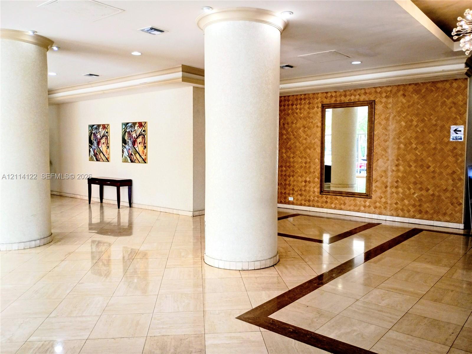 Spacious foyer featuring large-scale cylindrical architectural columns, polished stone flooring with decorative inlay, recessed ceiling lighting, and a textured accent wall Spacious foyer featuring large-scale cylindrical architectural columns, polished stone flooring with decorative inlay, recessed ceiling lighting, and a textured accent wall