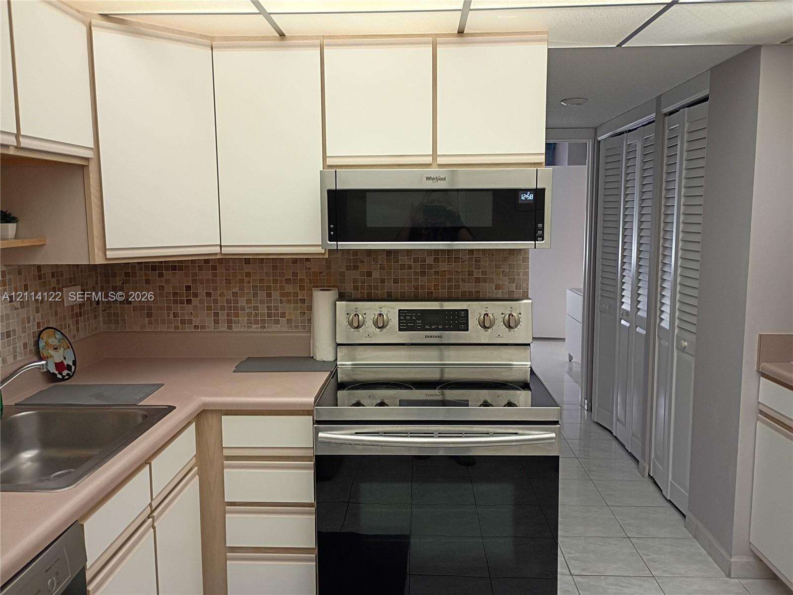 Kitchen featuring flat-panel cabinetry, stainless steel oven with range, matching over-the-range microwave, mosaic tile backsplash, and light-tone countertops