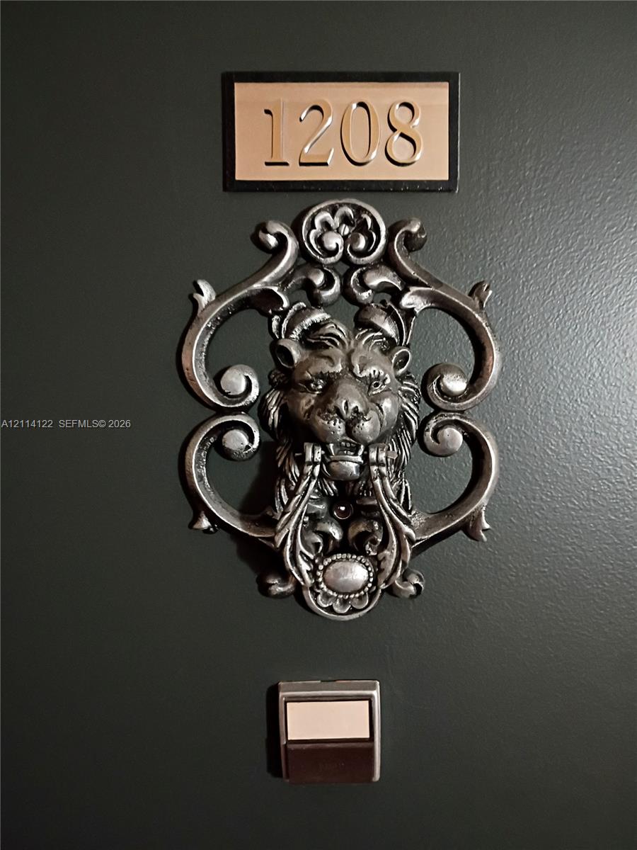Dark-toned entry door featuring a metallic lion-head door knocker, custom rectangular house number plaque, and a built-in metal doorbell button