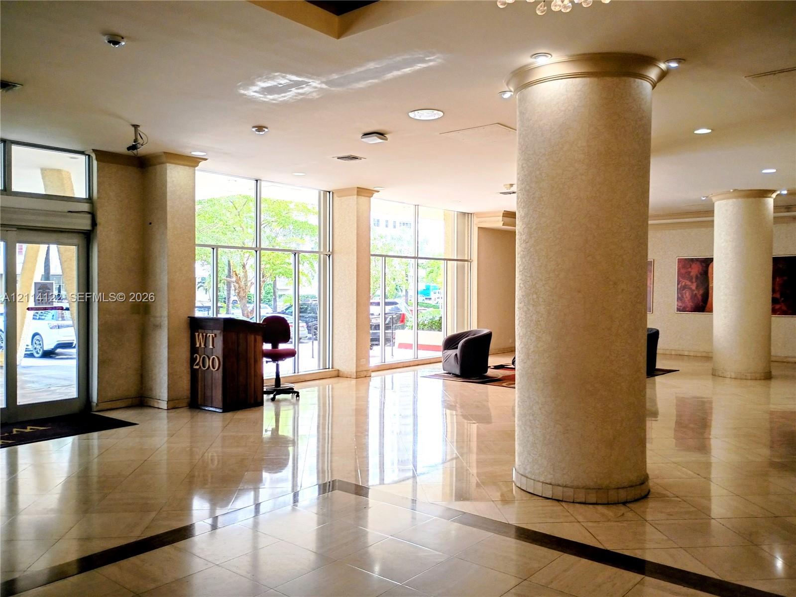 Lobby featuring floor-to-ceiling windows, polished stone tile flooring, structural columns, and recessed lighting Lobby featuring floor-to-ceiling windows, polished stone tile flooring, structural columns, and recessed lighting