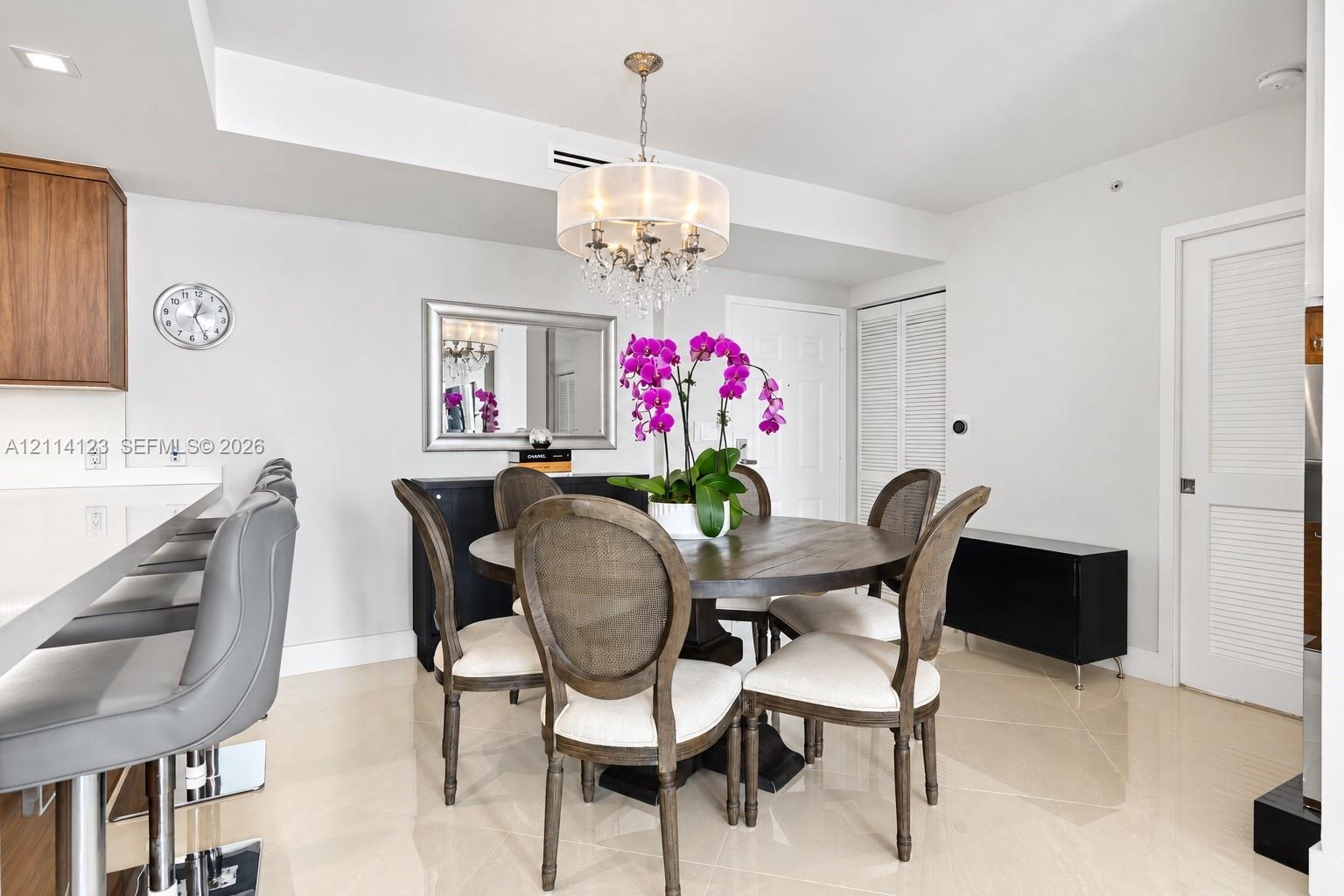 Dining space featuring a multi-tiered crystal chandelier, polished neutral tile flooring, and white recessed lighting