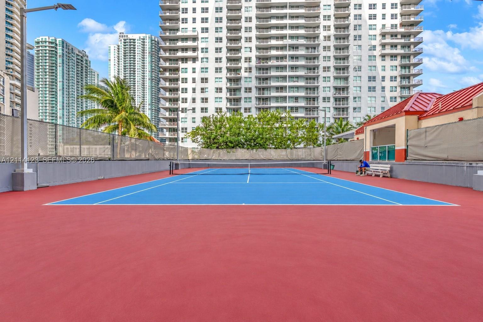 Tennis court featuring a high-contrast blue and red surface, perimeter fencing, and built-in lighting